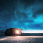 Aurora borealis over old small house with yellow light in window