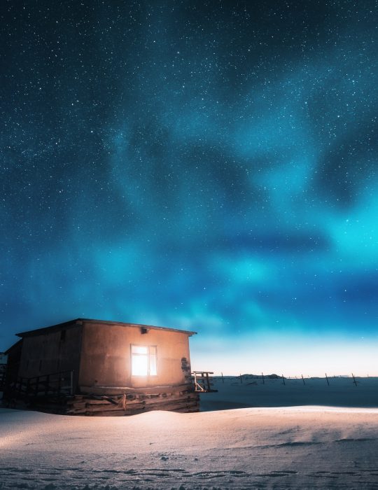 Aurora borealis over old small house with yellow light in window